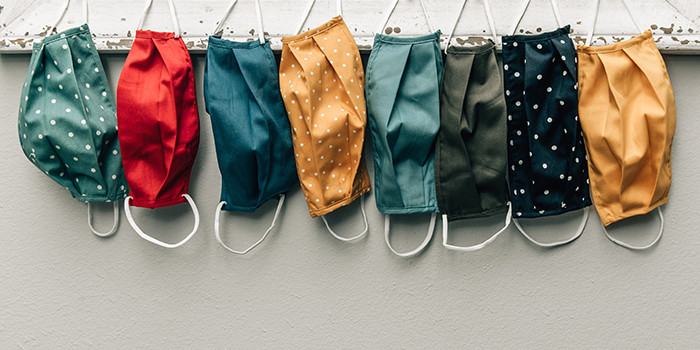 Row of colorful cloth masks hanging against neutral tone wall surface