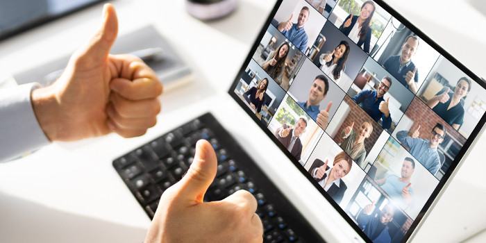 Image of video conference on device screen with man's hands displaying two thumbs up in gesture of approval