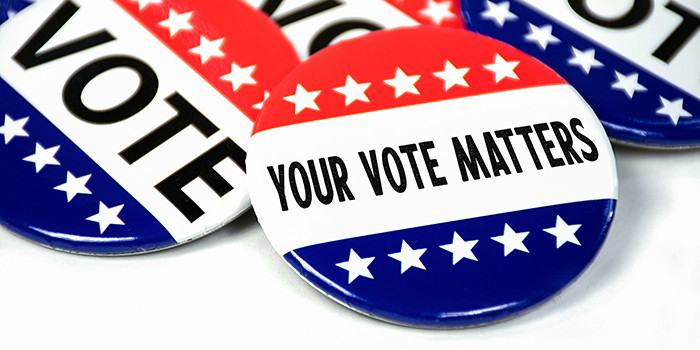 Photo of red white and blue patriotic buttons with white stars and black text reading VOTE and YOUR VOTE MATTERS