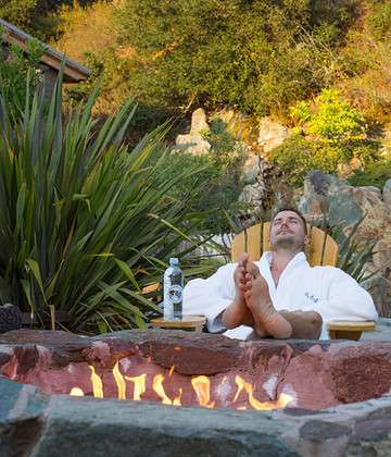 Image of a man reclining in a chair, feet up by the fire pit.