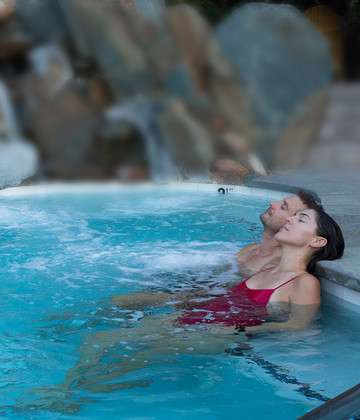 Image of a young couple in a Refuge hot pool, leaning back against the edge with their eyes closed.