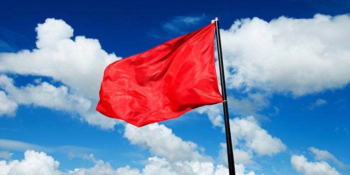 Red flag waving against blue sky (Adobe Stock)